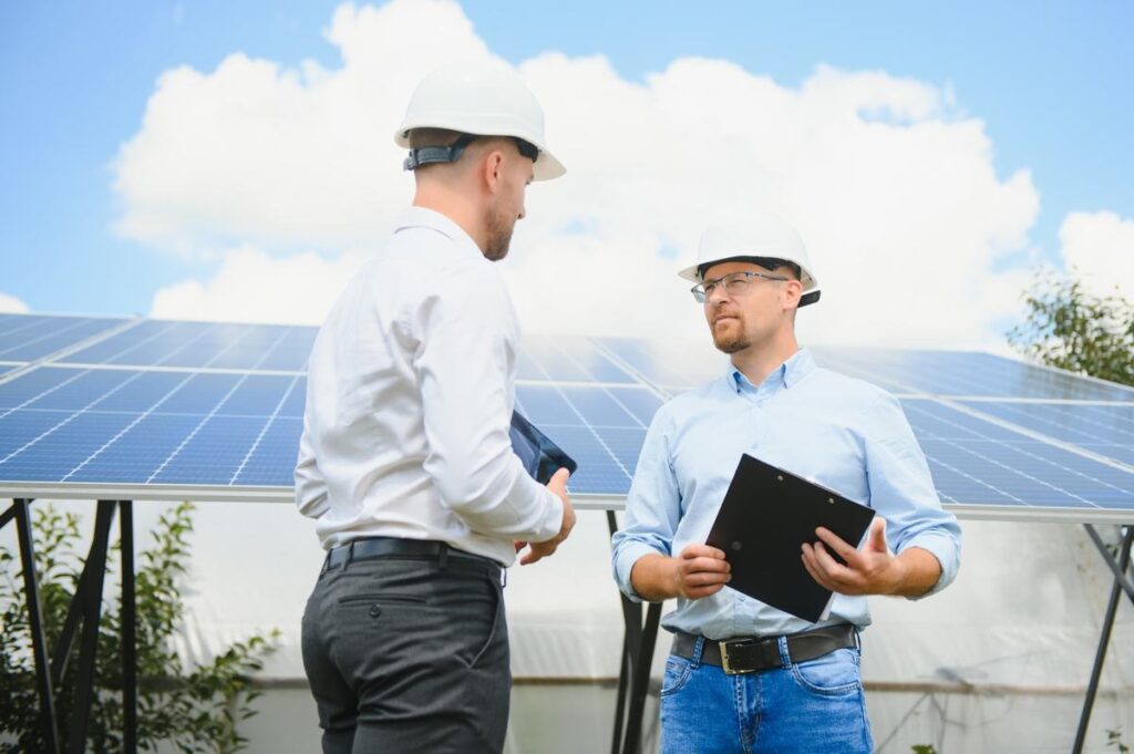 Solar technicians reviewing system performance on a laptop beside rooftop solar panels.